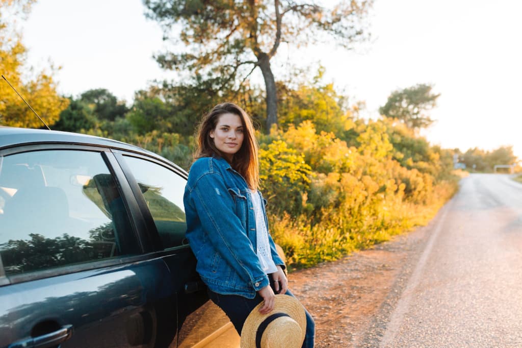 Girl with a hat in her hands near a car on the road