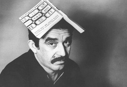 A black and white photo of a man with a book on his head