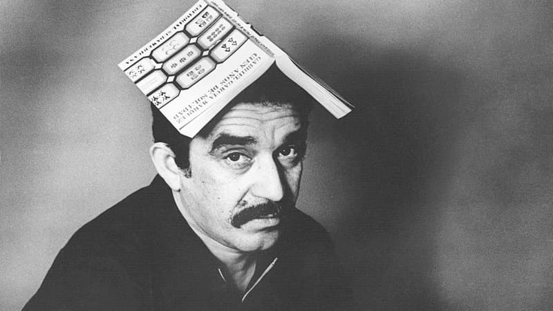 A black and white photo of a man with a book on his head